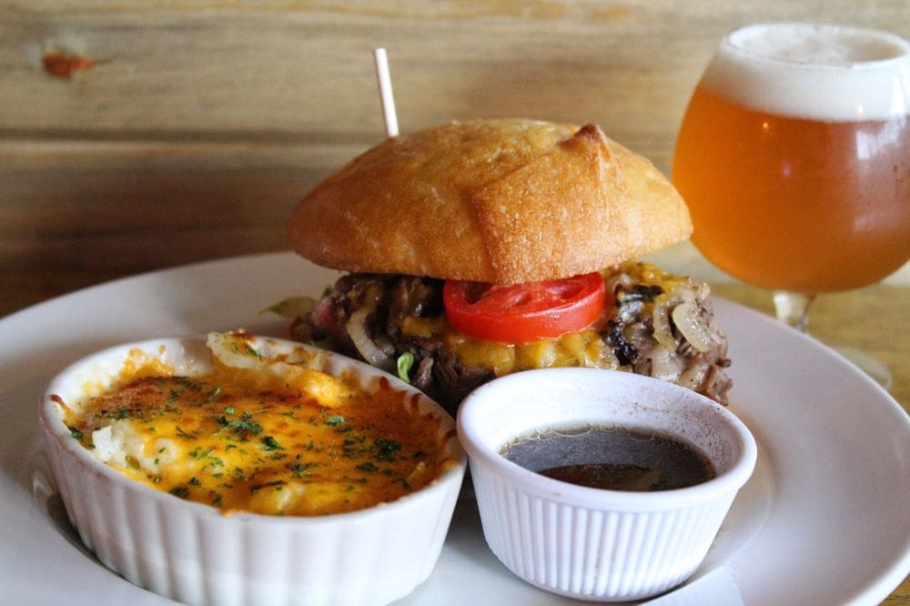 Plate with Hamburger with mushrooms, onions, and cheese and tomato, with a side dish of mac and cheese and au jus with glass of beer on side