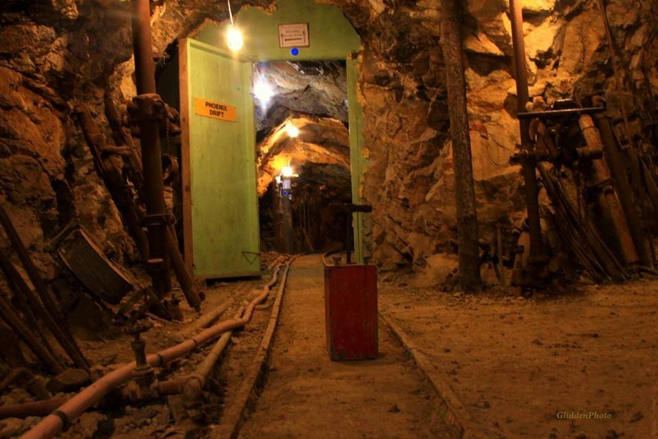 Underground mine with train tracks and green door, open to more rocky tunnel