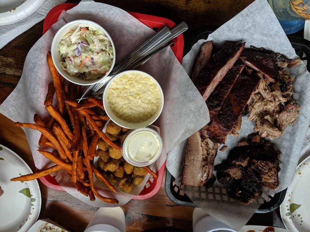 Bird's eye view of two baskets, one basket of four different smoked meats, the other with sweet potato fries, fried okra, mac and cheese and cole slaw